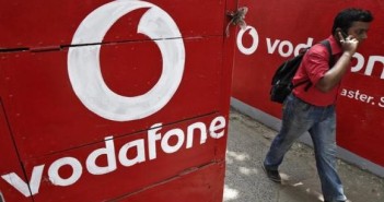 Man speaks on his mobile phone as he walks past the logos of Vodafone painted on a roadside wall in Kolkata